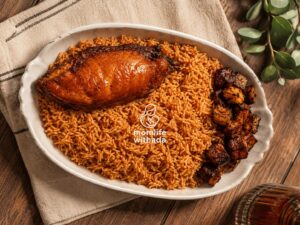 A pot of tasty smoky Nigerian Jollof Rice with steam rising, served in a white ceramic bowl garnished with fried plantain and a green salad on the side.