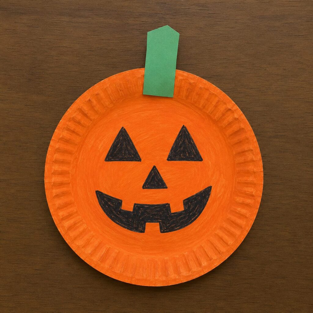 A paper plate painted orange with a green paper stem and jack-o-lantern face drawn in black marker